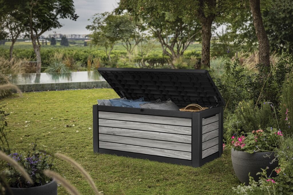 Skrzynia ogrodowa KETER Deco Deck Box 630 L Szary, polipropylen, wentylacja, trwałość, budowa, Kobieta przy otwartej skrzyni ogrodowej Deco wypełnionej poduszkami.
