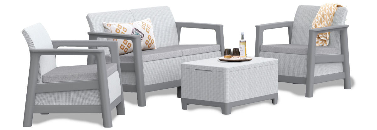 Zestaw mebli ogrodowych w jasnoszarym kolorze, składający się z dwóch foteli, sofy i stolika. Na stoliku znajdują się butelka i dwa kieliszki, a na sofie i jednym z foteli leżą poduszki i koc.