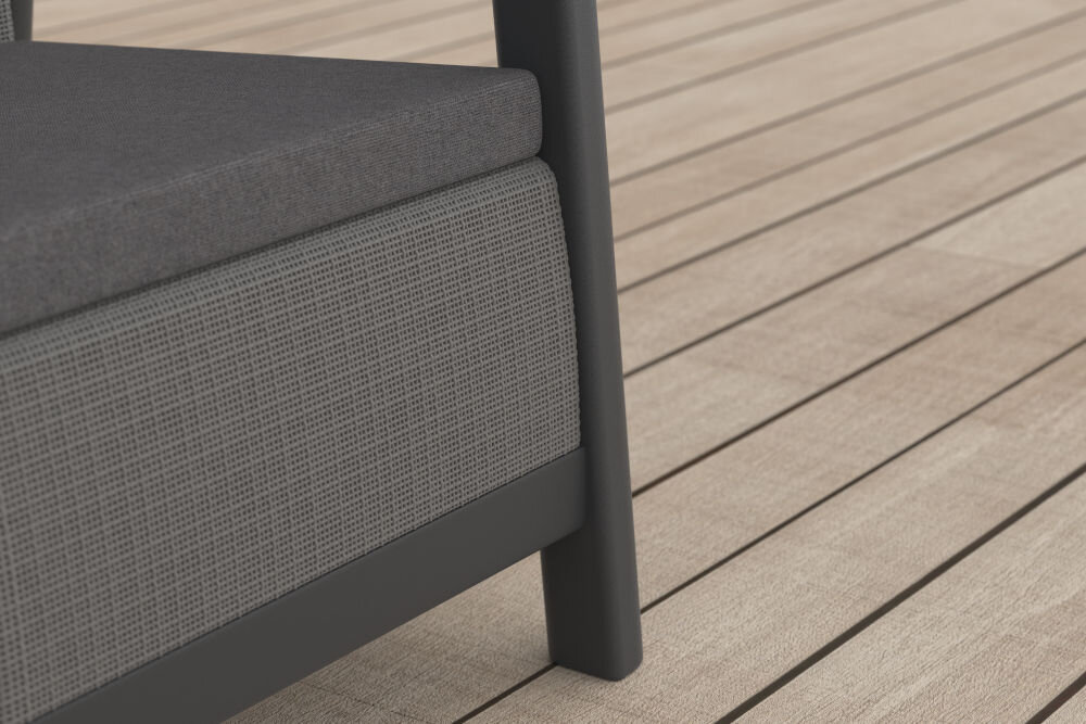 Fragment mebla ogrodowego z grafitowo-szarym siedziskiem i oparciem, ustawiony na drewnianej podłodze tarasowej. Konstrukcja mebla jest ciemna, a materiał siedziska ma teksturowaną powierzchnię.