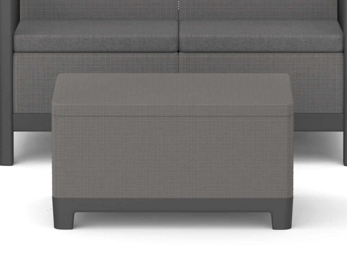 Na obrazie widoczny jest prostokątny, grafitowo-szary stolik ogrodowy z teksturowaną powierzchnią. W tle znajduje się fragment kanapy w podobnym kolorze.