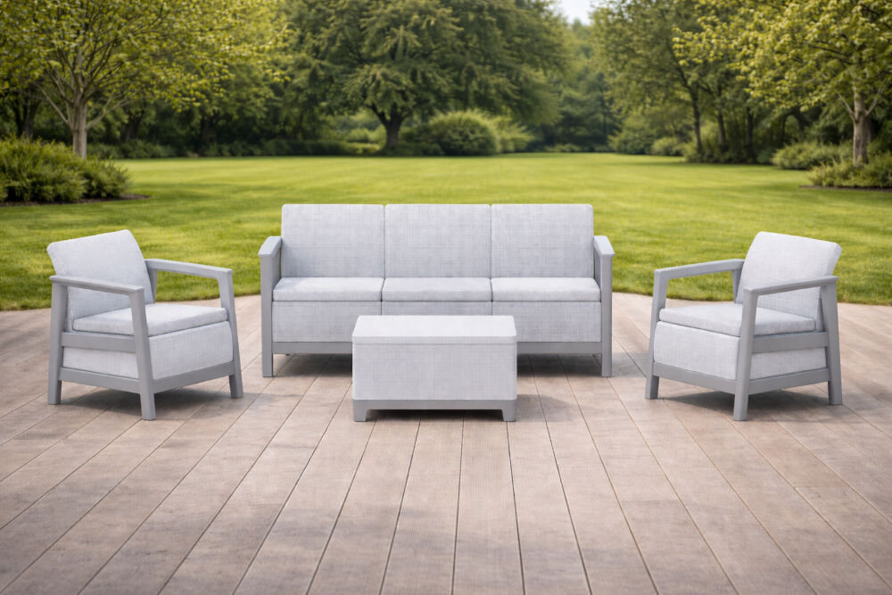 Zestaw mebli ogrodowych w jasnoszarym kolorze, składający się z sofy, dwóch foteli i stolika, ustawiony na drewnianym tarasie z widokiem na zielony trawnik i drzewa w tle.