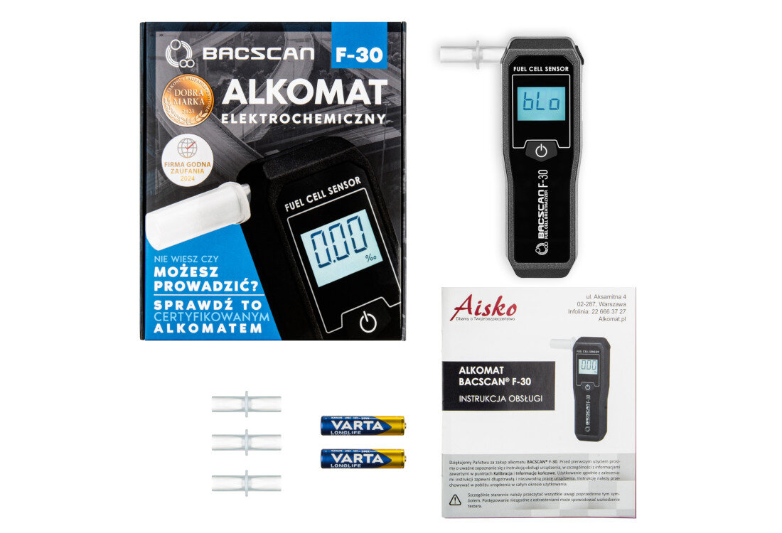Na obrazie znajduje się alkomat BACSCAN F-30 z wyświetlaczem pokazującym \'bl0\', opakowanie z napisem \'ALKOMAT ELEKTROCHEMICZNY\', instrukcja obsługi oraz dwie baterie VARTA. Widoczne są również ustniki do alkomatu.