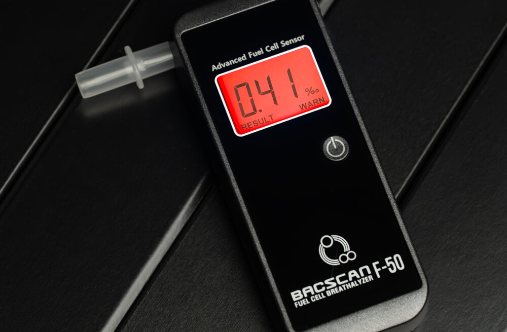 Na obrazie widoczny jest alkomat z wyświetlaczem pokazującym wynik 0.41‰. Na urządzeniu znajduje się napis \'BACSCAN F-50\' oraz \'Advanced Fuel Cell Sensor\'.