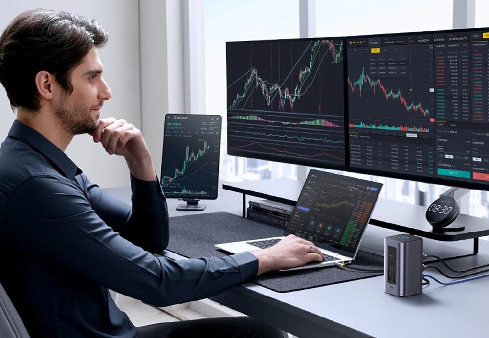 Stacja dokująca BASEUS NU1 Air Spacemate Mężczyzna w garniturze przy biurku z laptopem i dwoma monitorami pokazującymi wykresy finansowe, stacja dokująca stoi obok komputera