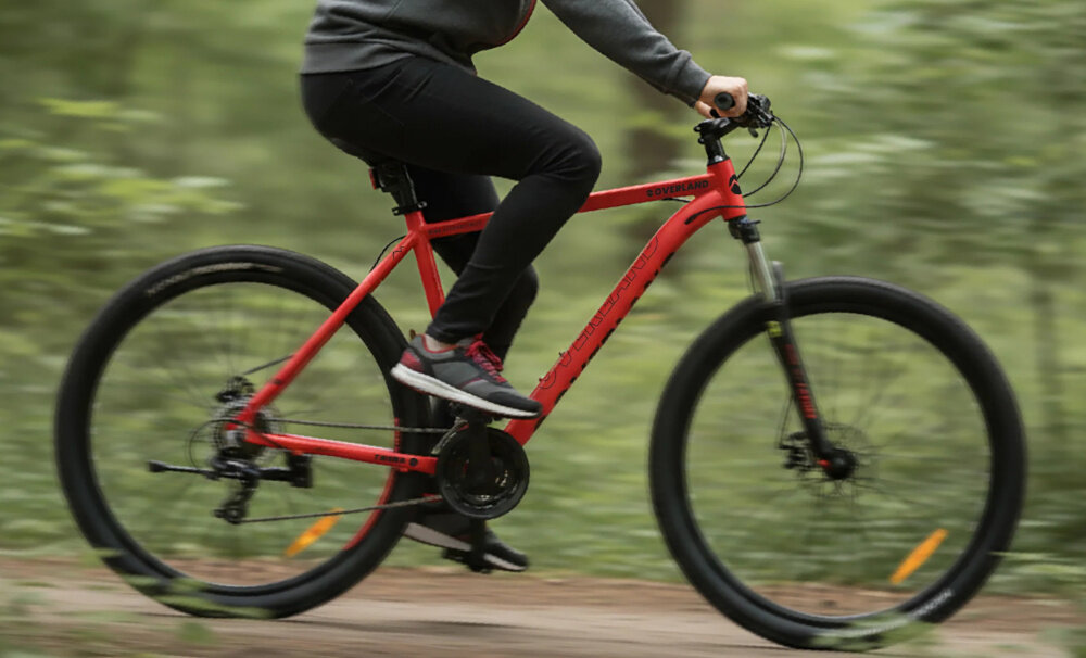 Rower górski MTB TATRA Overland U21 29 cali Czerwony las droga leśna osoba jedzie na rowerze w stroju sportowym widok z boku podstawa bezpieczeństwa hamulce tarczowe mechaniczne w każdych warunkach pogodowych i na każdej trasie bardzo dużą siłę hamowania z przodu i z tyłu podwójny pakiet bezpieczeństwa