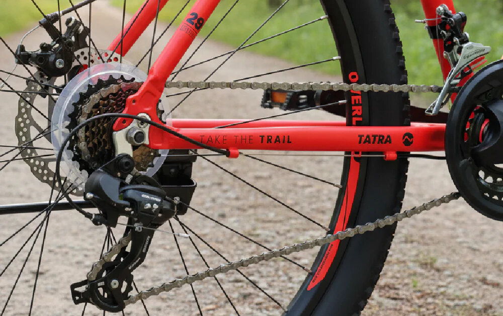 Rower górski MTB TATRA Overland U21 29 cali Czerwony las droga leśna zbliżenie na tylną przerzutkę przerzutki marki SHIMANO 21 przełożeń duża wytrzymałość sprawne działanie zmiana biegów jest płynna i bezproblemowa przednie i tylne przerzutki SHIMANO Tourney stabilność i precyzja precyzyjna praca mechanizmu