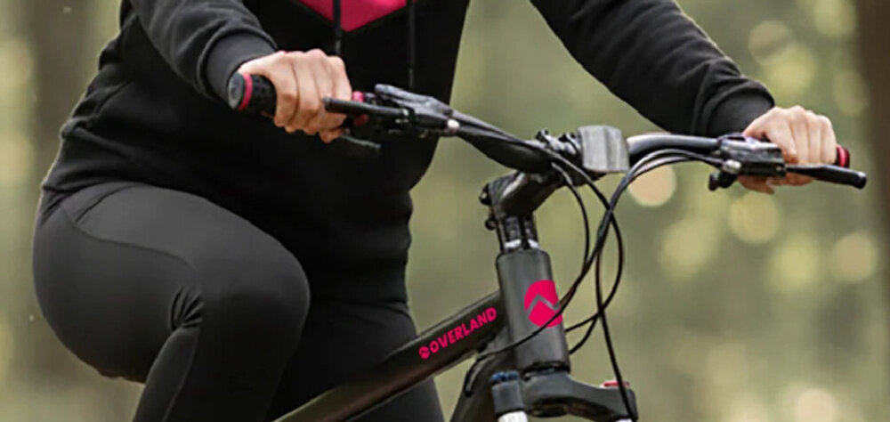 Rower górski MTB TATRA Overland U21 29 cali Czarno-fuksjowy las osoba na rowerze zbliżenie na kierownicę osoba trzyma dłonie na uchwytach kierownica MTB marki Ciclo Sport stalowy wspornik regulacja wysokości kierownicy w zakresie 97–99 cm kontrolowanie roweru wygodna pozycja