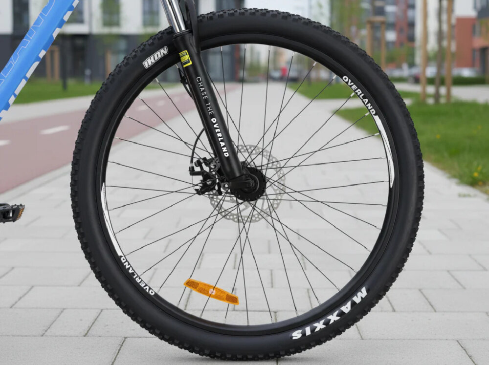 Rower górski MTB TATRA Overland U19 27.5 cala Niebieski chodnik zbliżenie na przednią oponę widok z boku opony marki MAXXIS w rozmiarze 27,5 cali głęboki bieżnik skutecznie wspiera jazdę ułatwia utrzymanie stabilnego toru jazdy aluminiowe obręcze stalowe piasty marki Ciclo Sport regularne sprawdzanie ciśnienia powietrza wartość na bocznej części opony