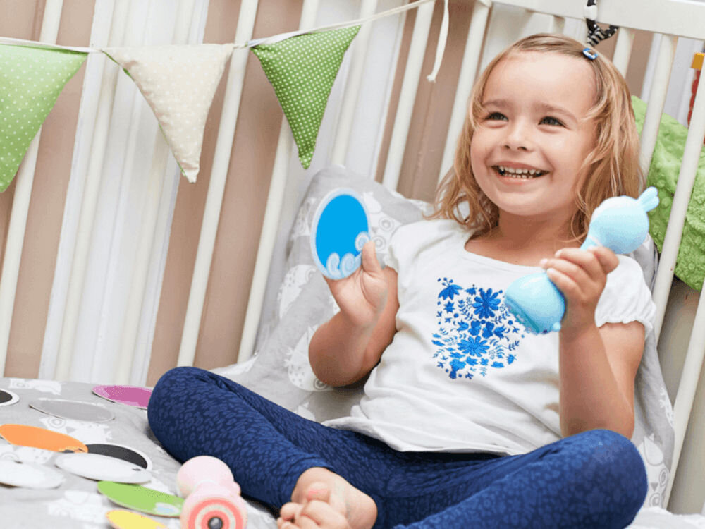 Zabawka edukacyjna ALILO Smarty Bunny R1 Niebieski edukacja z uśmiechem, dziewczynka siedząca w łóżeczku z zabawką w ręce