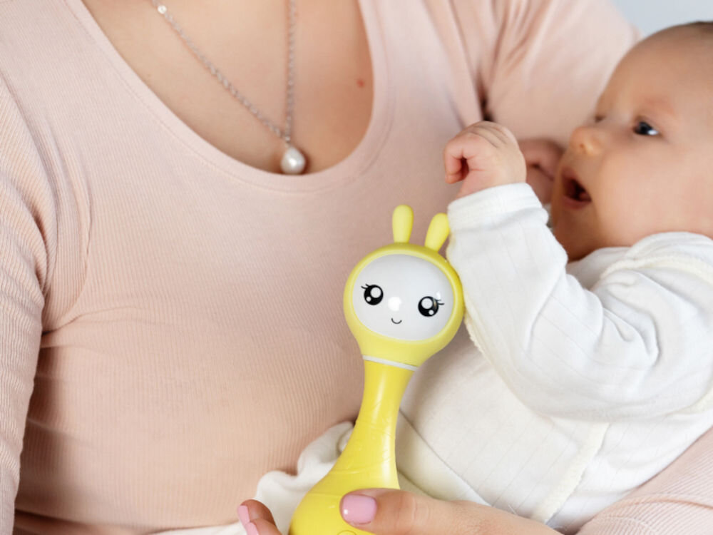 Zabawka edukacyjna ALILO Smarty Bunny R1 Niebieski muzyczne odkrycia malucha, funkcja elektronicznej grzechotki, 66 różnorodnych dźwięków, dobry sposób na rozwijanie słuchu i zmysłów malucha, bogactwo dźwięków,
					dziecko na rękach kobiety