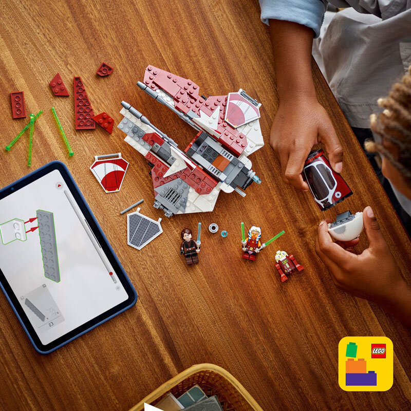 Na drewnianym stole znajdują się elementy zestawu LEGO, w tym części statku kosmicznego i trzy figurki. Obok leży tablet z instrukcją budowy, a w rogu widoczne jest logo LEGO.