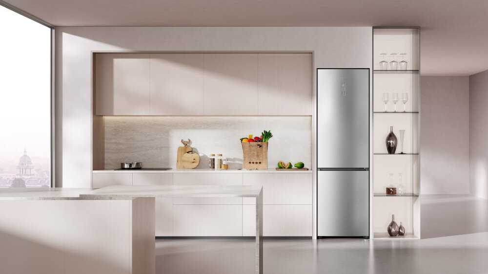 LODÓWKA DREAME COMBI MegaPro 2M-C DRB450WMBCEU NO FROST 201cm INOXZdjęcie przedstawia minimalistyczną kuchnię w jasnych odcieniach. Po prawej stronie znajduje się lodówka wolnostojąca w kolorze srebrnym, zintegrowana wizualnie z wysoką zabudową i otwartymi półkami na szkło oraz dekoracje. Wnętrze jest przestronne, dobrze doświetlone, a całość podkreśla elegancki design urządzenia i jego dopasowanie aranżacji kuchennych