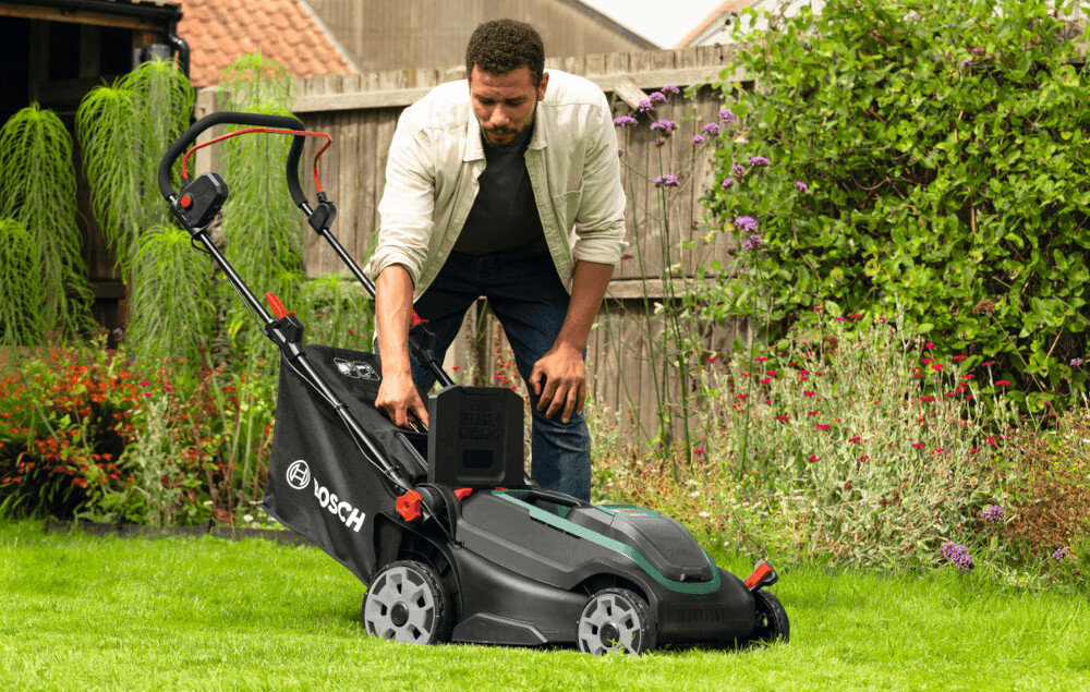 Osoba obsługuje kosiarkę akumulatorową na trawniku. Na kosiarce widoczne jest logo BOSCH.