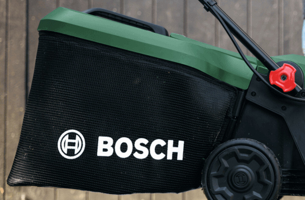 Czarna torba na trawę z logo BOSCH przymocowana do zielonej kosiarki z widocznym kołem i uchwytem.