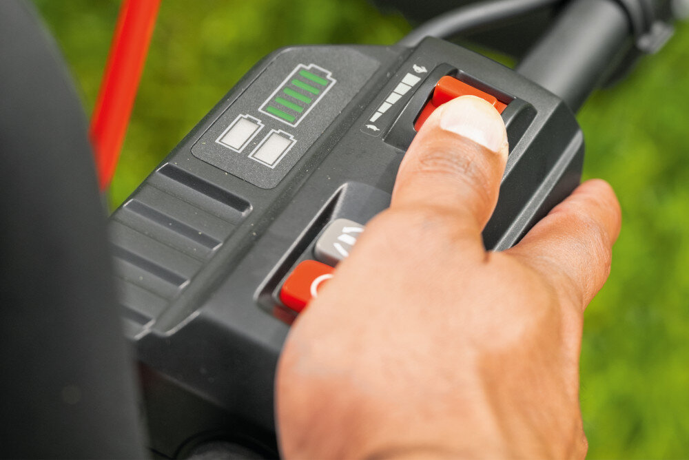 Kosiarka akumulatorowa BOSCH Professional GRA18V2-46SP 06008C8200 zbliżenie na uchwyt osoba trzyma dłoń na przycisku do regulacji prędkości szerokość robocza 46 cm redukuje liczbę przejść podczas pracy napęd z płynną regulacją prędkości od 2 do 6,4 km/h automatyczne wspomaganie jazdy urządzenie porusza się samodzielnie równomierne tempo pracy zmniejsza zmęczenie ułatwia prowadzenie kosiarki