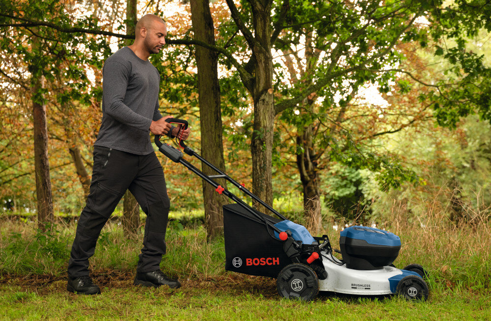 Kosiarka akumulatorowa BOSCH Professional GRA18V2-46SP 06008C8200 ogród osoba kosi trawę widok z boku w tle drzewa 60-litrowy kosz ogranicza konieczność częstego opróżniania dłuższa bardziej płynna praca z wysokiej jakości materiału tekstylnego 