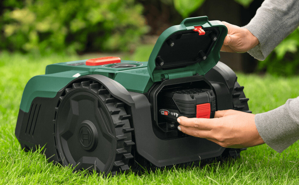 Robot koszący  BOSCH Visimow 18V-100 06008E1001 Bez przewodu ograniczającego ogród trawnik robot stoi na trawniku osoba wkłada akumulator w miejsce do tego przeznaczone zasilany wymiennym akumulatorem z serii BOSCH Power For All 18 V pozwala zasilać wiele narzędzi jednym akumulatorem niezależność od źródła zasilania