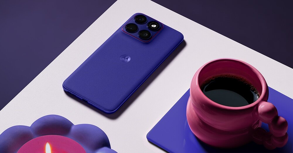 Na stole leży fioletowy smartfon z trzema aparatami, obok znajduje się różowa filiżanka na fioletowej podstawce oraz świeczka w fioletowym świeczniku. Na obudowie telefonu widoczne jest logo producenta.