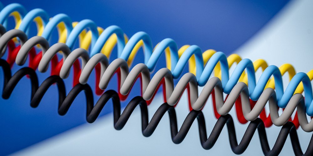 Silikonowe, spiralne kable Newell USB-C - USB-C 100 W, 1,5m w różnych kolorach na niebieskim tle.