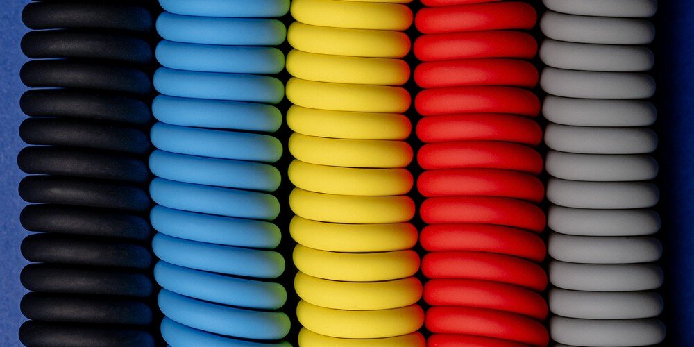 5 silikonowych kabli spiralnych Newell USB-C - USB-C 100 W, 1,5m na niebieskim tle. Każdy z nich w innym kolorze.