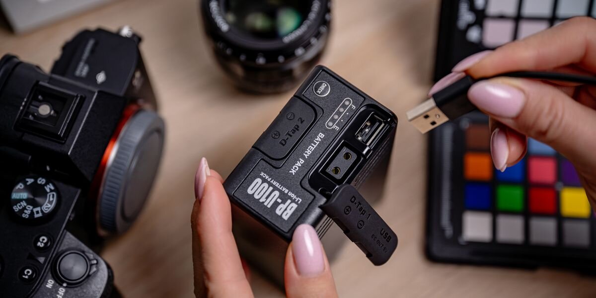 Akumulator NEWELL 6700 mAh BP-U100 do Sony, Zbliżenie na otwartą gumową zaślepkę akumulatora, odsłaniającą gniazda USB oraz D-Tap, z kablem USB w tle, PXW, PMW, złącza, 70×40×104