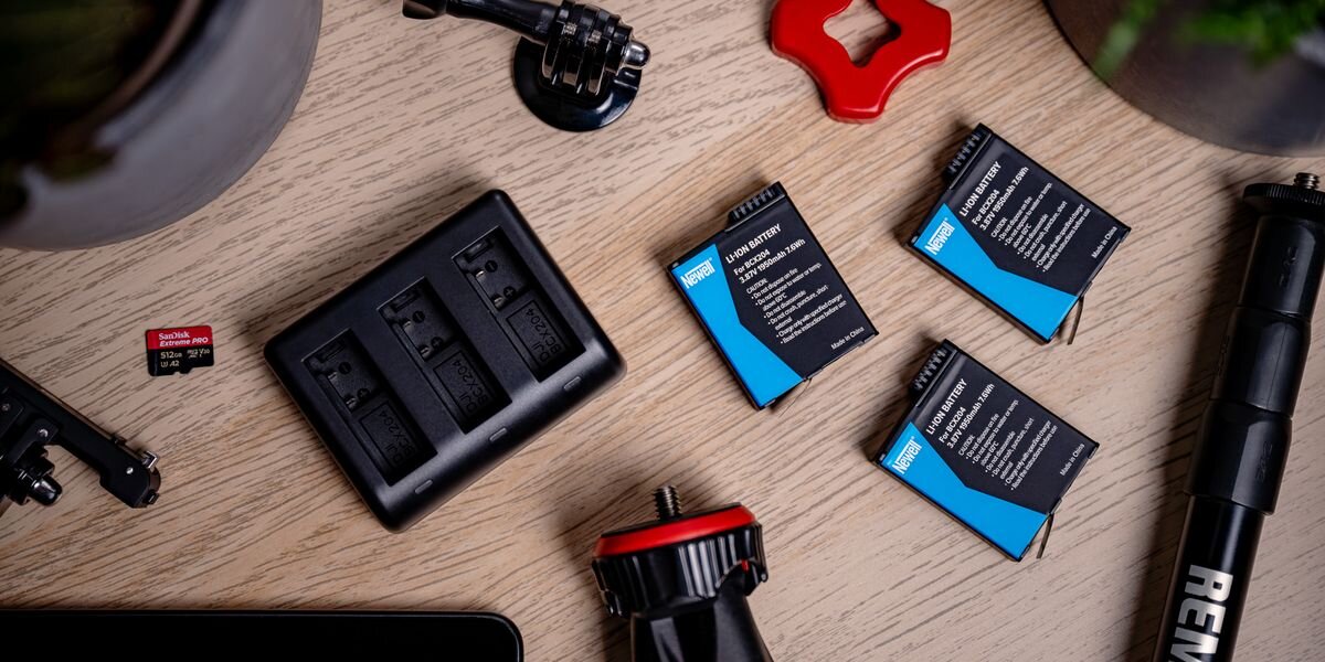 Ładowarka trzykanałowa NEWELL SDC-USB-C + 3 akumulatory BCX-204 do DJI Osmo Action, Na drewnianym blacie leży ładowarka trzykanałowa oraz trzy akumulatory i akcesoria do kamery sportowej, pod ręką, energia, zasilanie, bateria