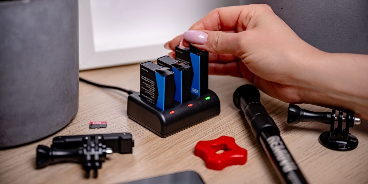 Ładowarka trzykanałowa NEWELL SDC-USB-C + 3 akumulatory BCX-204 do DJI Osmo Action, Dłoń umieszcza akumulator w ładowarce, widoczne diody LED oraz akcesoria do kamery sportowej, ładowanie, mobilność, USB, energia