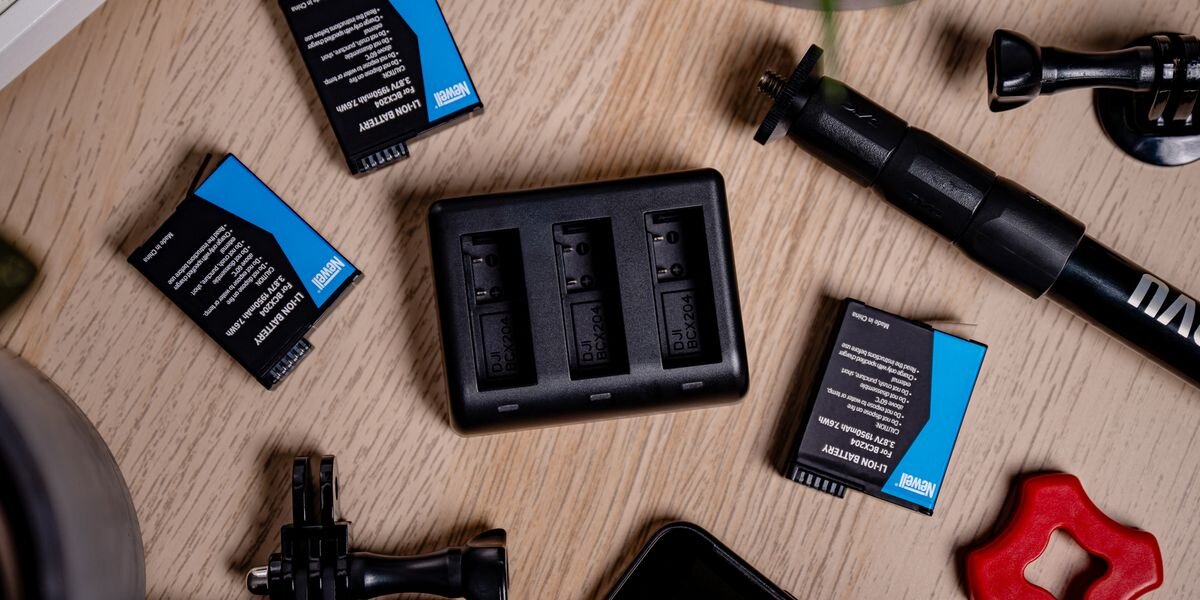 Ładowarka trzykanałowa NEWELL SDC-USB-C + 3 akumulatory BCX-204 do DJI Osmo Action, Ładowarka trzykanałowa na środku, wokół akumulatory i akcesoria do kamery na drewnianej powierzchni, mobilność, sprzęt, podróż, ergonomia