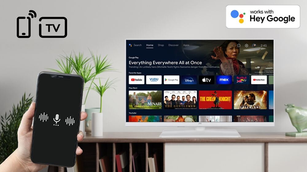 Telewizor JVC LT-32VAF330W Asystent Google sterowanie głosowe, telewizor stojący na komodzie w pomieszczeniu, ręka trzymająca smartfona