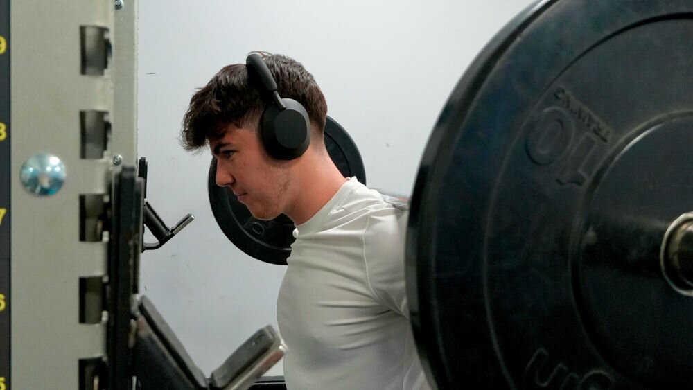 Słuchawki nauszne SONY WH-1000XM5SA z komfortowymi poduszkami i regulowanym pałąkiem, osoba z założonymi słuchawkami nausznymi robiąca trening z ciężarami