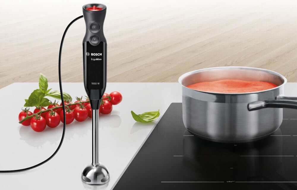 Blender BOSCH ErgoMixx MS61B6150 czarny blender czerwone pokrętło przyciski końcówka miksująca blender stoi na blacie obok na kuchence w garnku znajduje się zupa  mocny silnik 1000 W system QuattroBlade cztery stalowe ostrza blendowanie twardych składników ergonomiczny uchwyt specjalna stopka miksująca materiały bez BPA do codziennych zadań kulinarnych