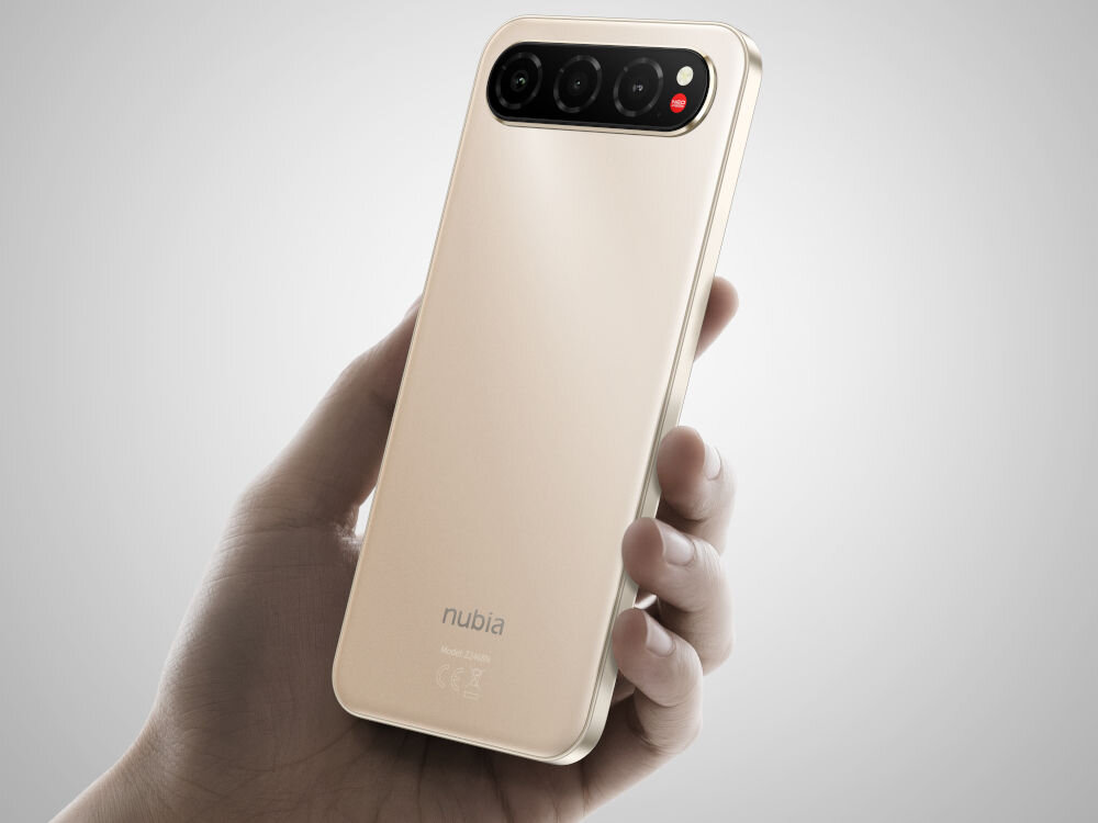 Smartfon NUBIA Air 8/256GB 6.78 120Hz Ręka trzyma smartfon nubia w kolorze złoto-beżowym (sand gold) pokazany tyłem. Widoczny jest podłużny, potrójny moduł aparatu z czerwonym akcentem.