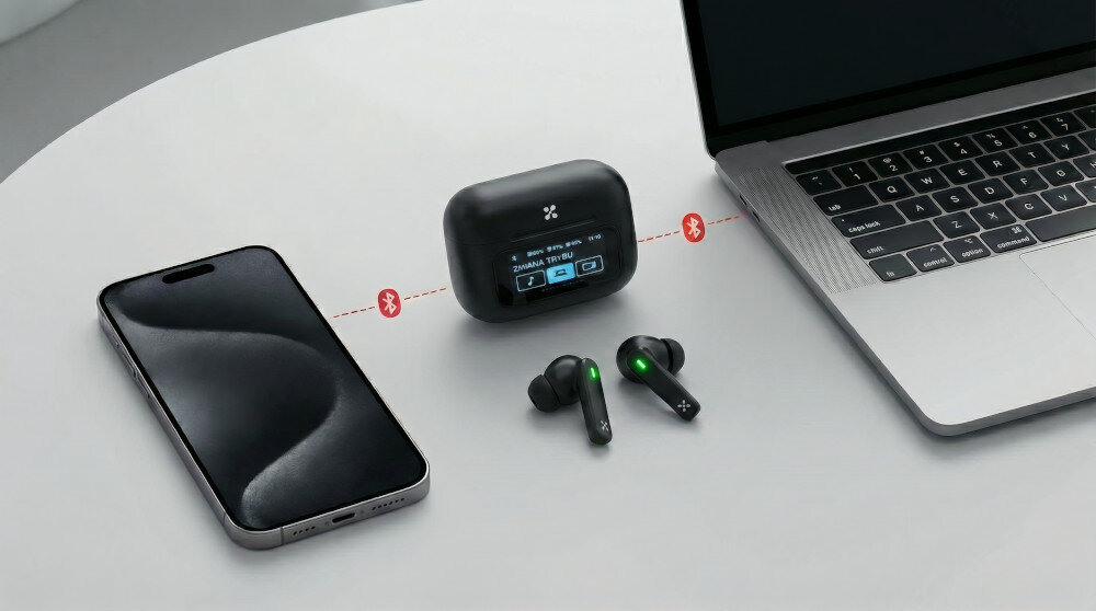 Na stole znajdują się słuchawki dokanałowe w kolorze białym, obok etui z wyświetlaczem pokazującym ikonę Bluetooth i poziom naładowania. Obok leży smartfon i laptop, a między nimi widoczne są ikony Bluetooth.