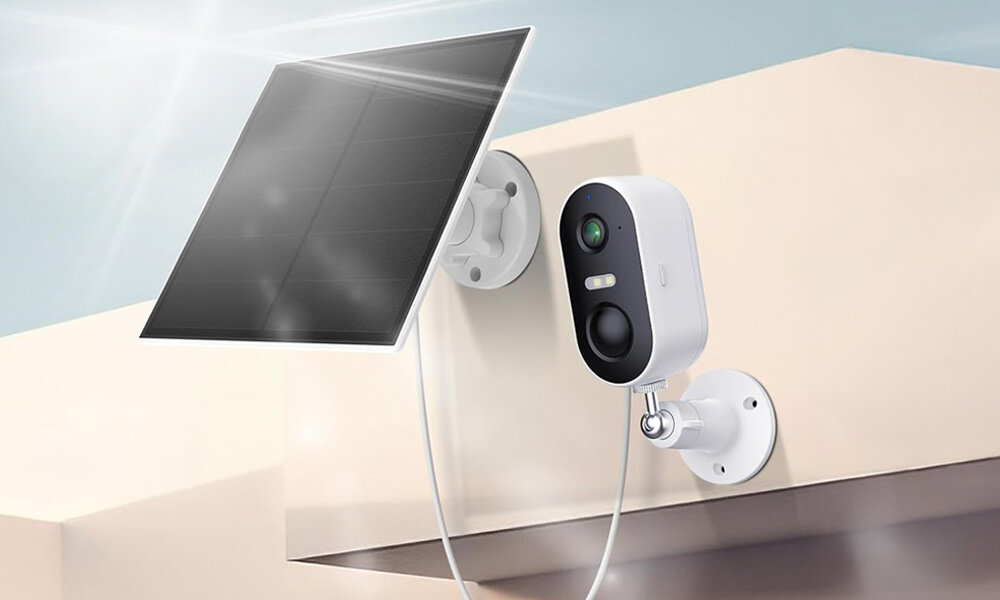 KKamera ARENTI GO1T Zewnętrzna, Wi-Fi + Panel solarny  Na beżowej ścianie nowoczesnego budynku wisi kamera Arenti z panelem solarnym. Grafika pokazuje jasne promienie słońca. czujnik PIR ruch do 10 metrów w kącie 120°