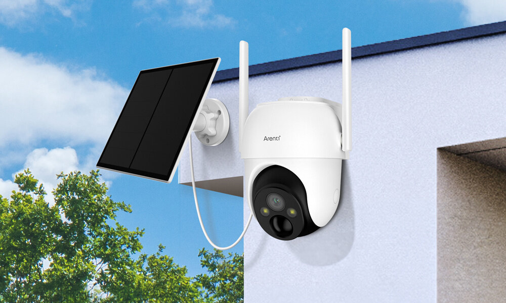 Kamera ARENTI GO2T Zewnętrzna, Wi-Fi, Kamera obrotowa + Panel solarny Na białym budynku zamontowana jest obrotowa kamera Arenti. Obok niej znajduje się połączony kablem panel solarny.