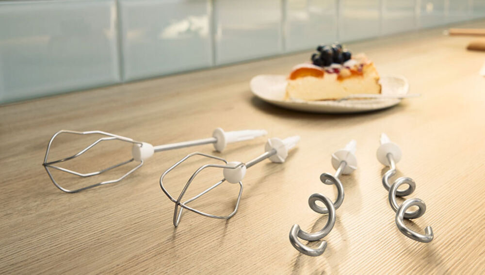 Mikser BOSCH ErgoMixx MFQ36465 Biały na blacie leżą cztery końcówki obok stoi kawałek ciasta Wysokiej jakości akcesoria proste przyjemne miksowanie, ubijanie i zagniatanie solidne mieszadła ze stali nierdzewnej sztywne białka lekkie jednolite ciasta wytrzymałe haki do zagniatania wyrabianie ciasta drożdżowego chlebowego makaronowego funkcjonalne narzędzia