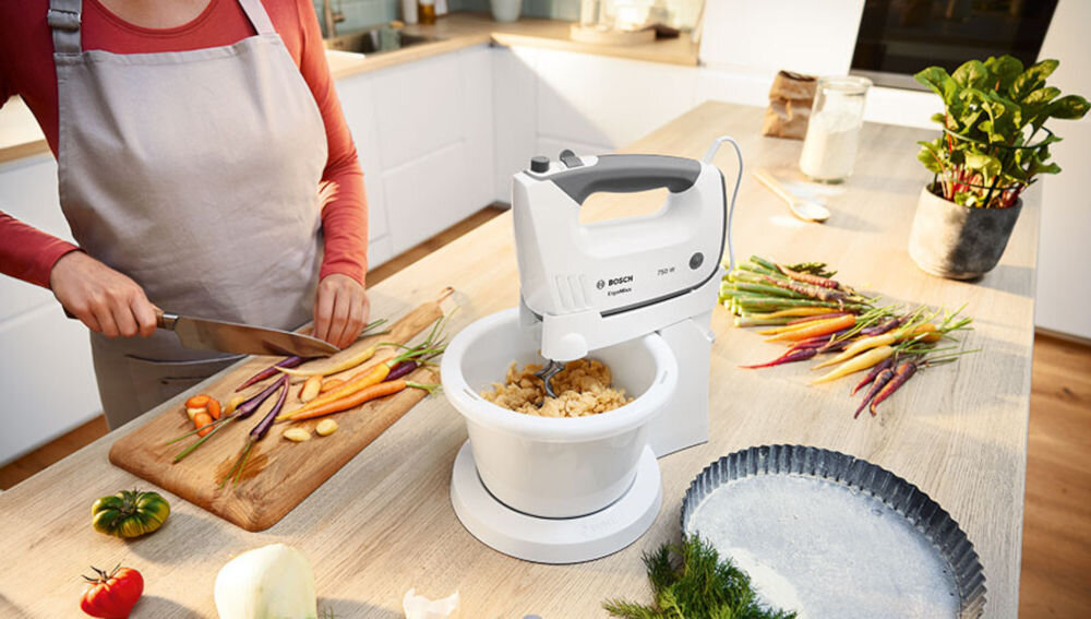 Mikser BOSCH ErgoMixx MFQ36465 Biały mikser stoi na blacie wyrabianie ciasta biała obudowa misa szare elementy osoba kroi warzywa na desce stojak misa obsługa bez użycia rąk optymalne rezultaty automatycznie obracająca się misa równomierne dokładne połączenie składników szybki łatwy efektywny proces wygoda wysoka jakość wypieków 