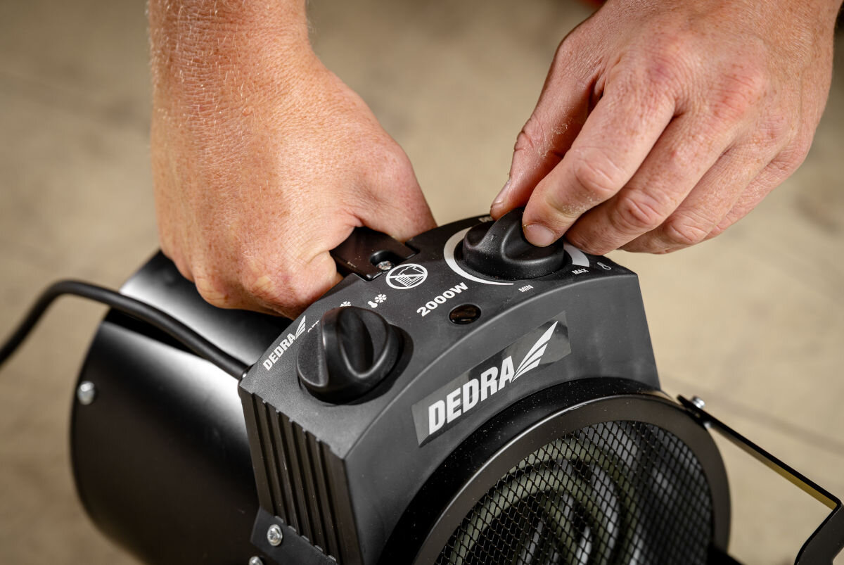 Nagrzewnica elektryczna DEDRA DED9930B, pokrętło, termostat, uniwersalność, oszczędność, Ręce ustawiają pokrętłem moc ogrzewania na panelu nagrzewnicy Dedra DED9930B, widok z góry.