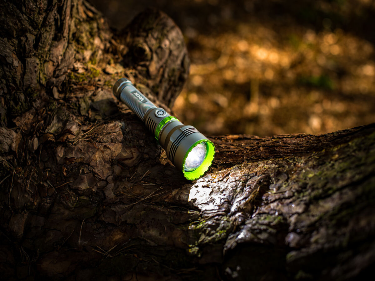 Latarka taktyczna VAYOX VA0363, Latarka na ciężkie warunki, Latarka włączona, leży na pniu drzewa wieczorową porą