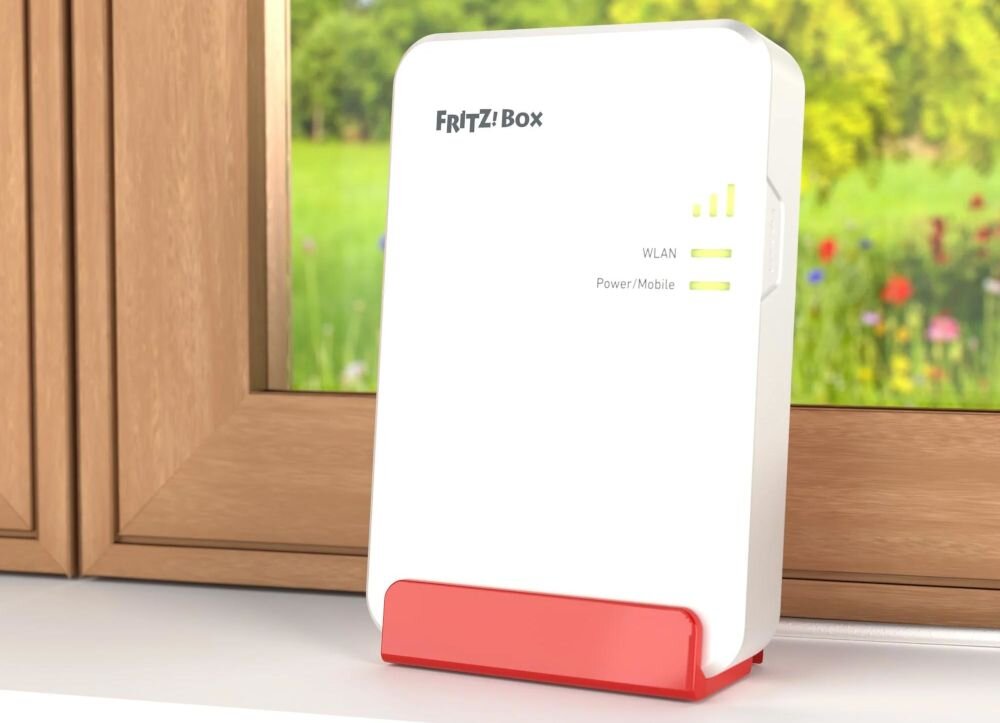 Repeater FRITZ!Box z Wi‑Fi stoi na parapecie przy oknie, rozszerzając zasięg sieci bezprzewodowej w domu.