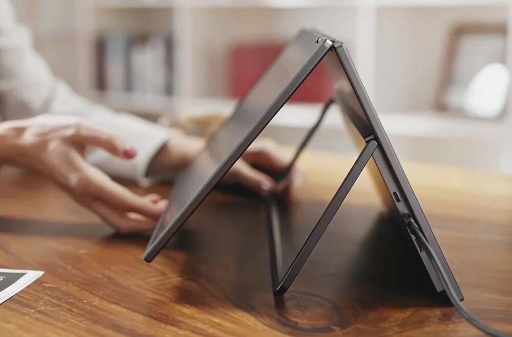 Monitor ACER PD163QT Zbliżenie z boku na dłonie opierające na drewnianym stole dwa połączone pod kątem ekrany z rozłożoną metalową podpórką i wpiętym kablem