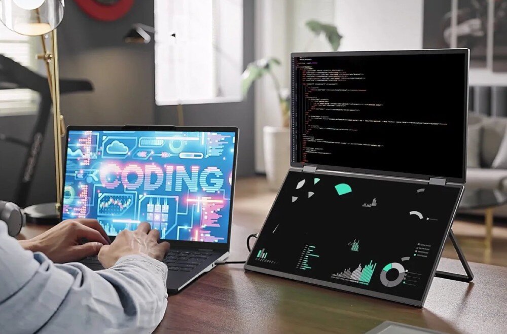 Monitor ACER PD163QT Mężczyzna piszący na laptopie z napisem 'CODING', obok którego stoją dwa pionowe ekrany wyświetlające linie kodu oraz wykresy kołowe na ciemnym tle