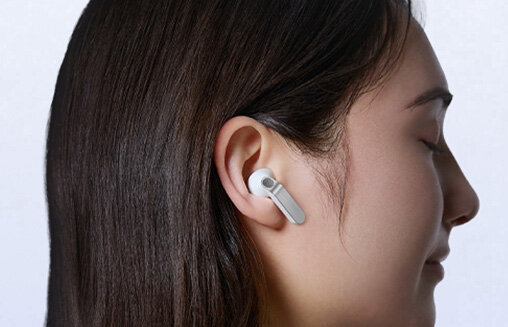Zbliżenie białych Galaxy Buds 4 z metalowymi krawędziami; scena zmiana, osoba w nich patrzy w prawo. Osoba nosi białą słuchawkę douszną w uchu.