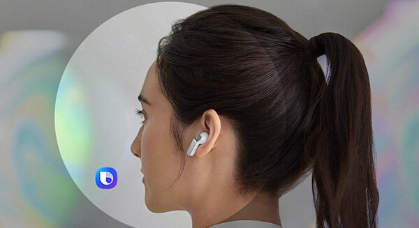 Tył osoby w białych Galaxy Buds4; ikona Bixby pokazuje AI do natychmiastowych odpowiedzi. Osoba z ciemnymi włosami spiętymi w kucyk nosi białe słuchawki douszne. W tle widoczne jest logo w kształcie litery \'b\'.