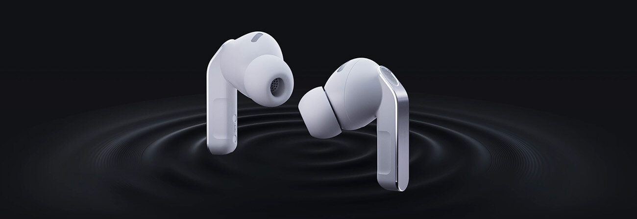 Elementy Galaxy Buds4Pro, m.in. woofer, trafiają do obudowy; gotowa słuchawka obraca się obok lewej. Na obrazie widoczne są dwa białe słuchawki dokanałowe na ciemnym tle, z falami dźwiękowymi wokół nich.