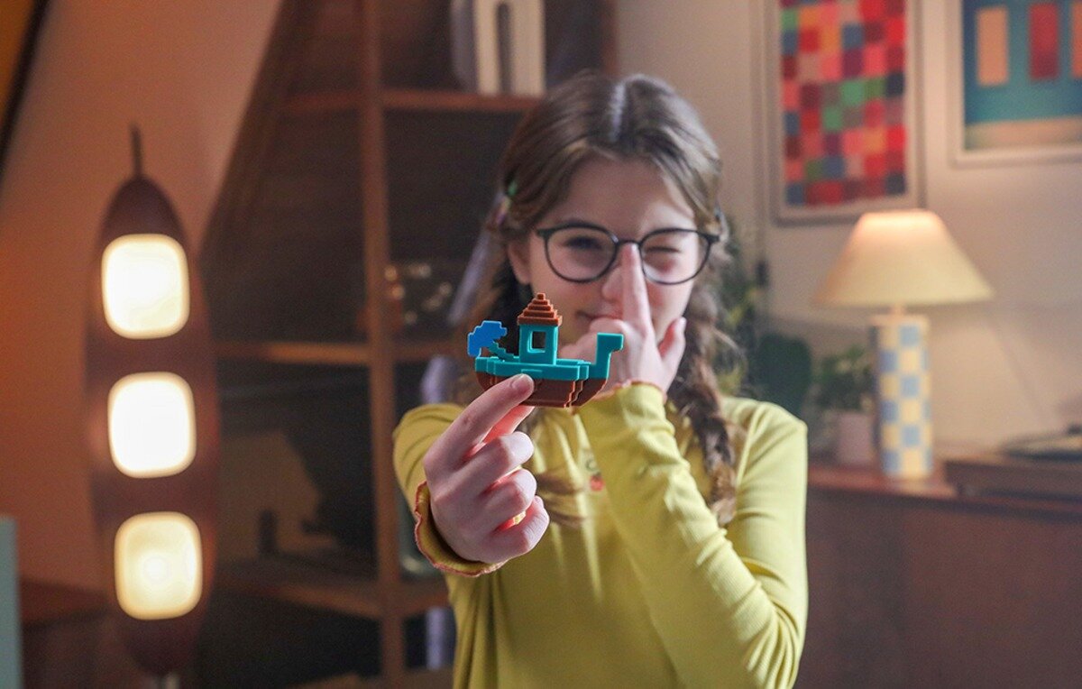 Dziewczynka w okularach trzyma w dłoni mały, plastikowy model łódki
