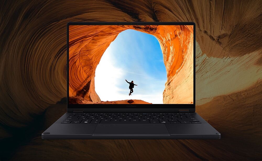 Laptop z wyświetlaczem pokazującym osobę skaczącą w skalnym łuku na tle nieba. Obudowa laptopa jest ciemna, a klawiatura jest widoczna.