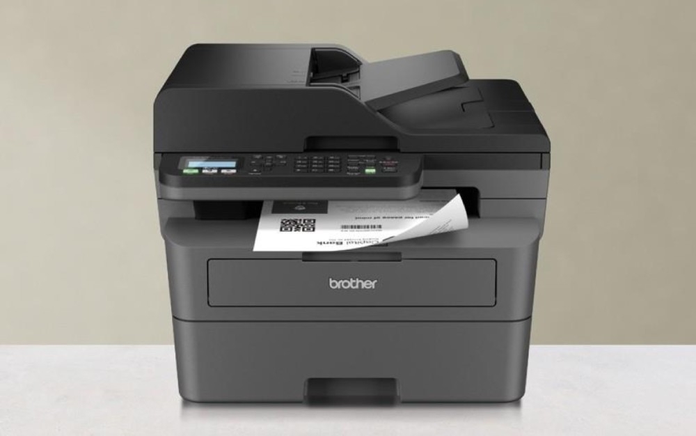 Urządzenie wielofunkcyjne BROTHER MFC-L2802DW urządzenie stojące przodem z widoczną kartką wychodzącą z niego podajnik taca odbiorcza formaty
