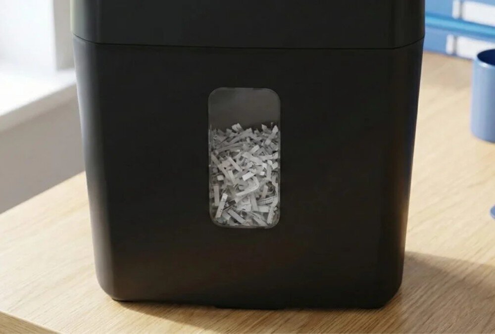 Niszczarka ścinkowa do dokumentów SAVIO ND-01 Zbliżenie na przednią ściankę czarnej niszczarki z przezroczystym okienkiem, przez które widać poziom zapełnienia kosza pociętym papierem