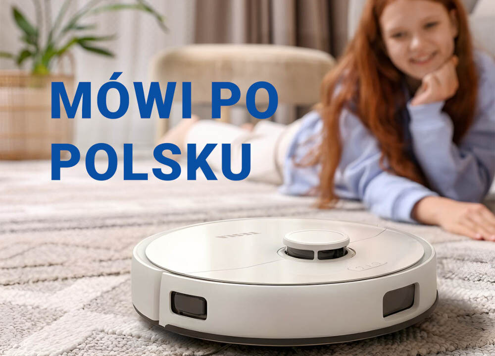 Na dywanie znajduje się biały robot sprzątający z widocznym logo TESLA. Obok widoczny jest napis \'MÓWI PO POLSKU\'.